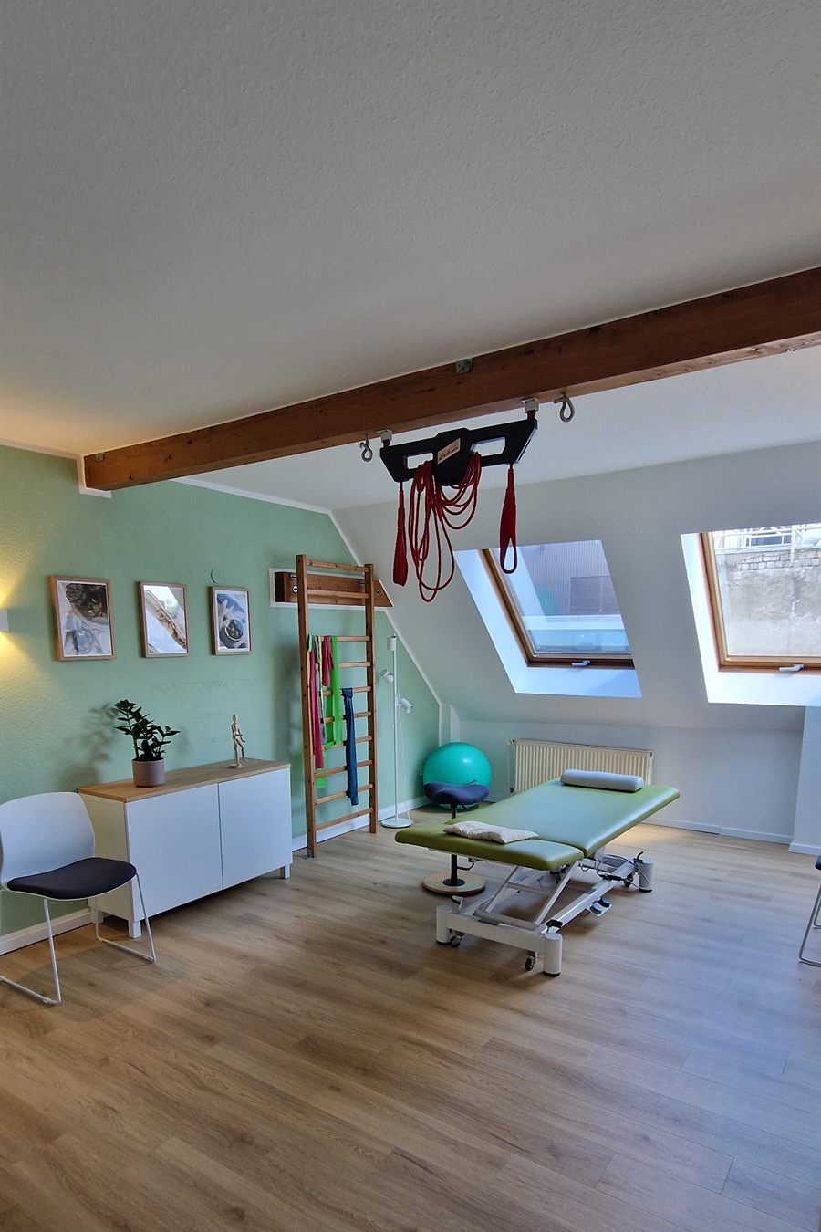 Therapieraum mit Behandlungsliege, Sprossenwand, Gymnastikball und Therapiebändern.